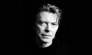 Foto em preto e branco do rosto de David Bowie olhando para a câmera em um fundo completamente preto.